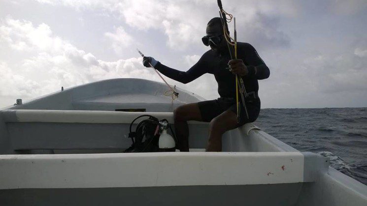 On the Placencia Producers' Cooperative boat, Elroy, a member of the team, is getting ready to spear some lionfish!